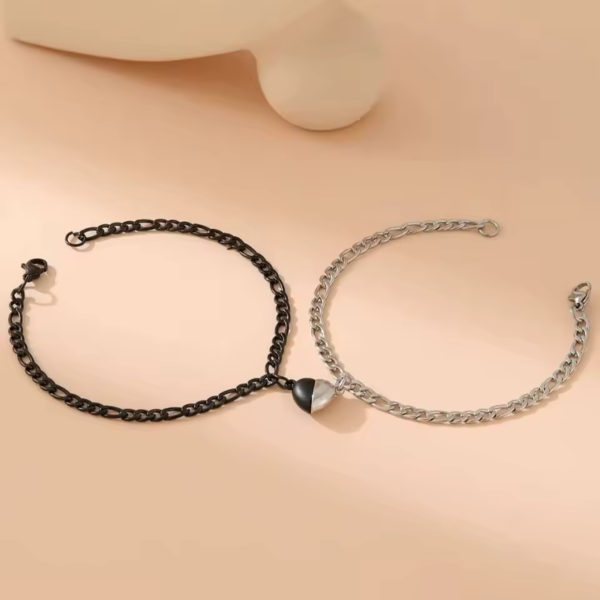 Bracelets couple aimantés en acier inoxydable noir et argenté, disposés sur une surface beige, avec leur pendentif magnétique en forme de cœur au centre.