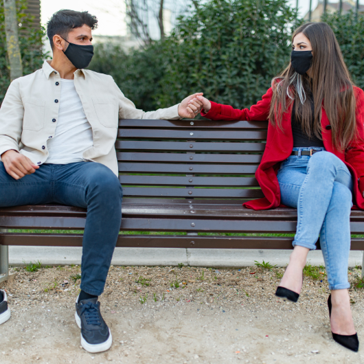 Couple portant des masques et se tenant la main à distance sur un banc, illustrant