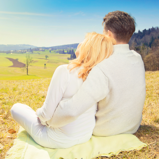 Un couple assis dans un champ, regardant l’horizon, illustrant l’amour et la connexion à distance grâce aux jeux en couple.