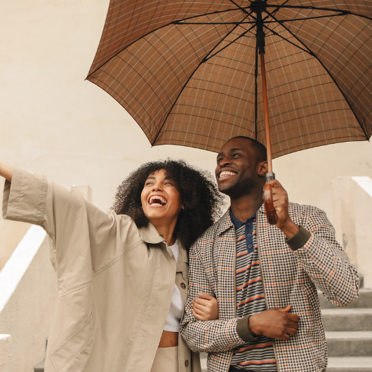 Couple souriant sous un parapluie en pleine pluie, profitant d’un moment complice