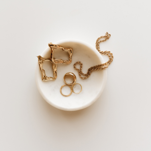 Des bijoux dorés élégamment présentés dans une coupelle, parfaits pour offrir à son partenaire lors d’une occasion spéciale.
